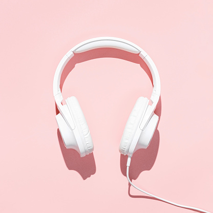 Flat lay white headphones on modern pale pink table wallpaper. Free space for creative design text and content.