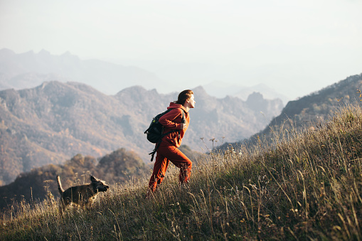 Beautiful woman traveler climbs uphill with a dog on a background of mountain views.