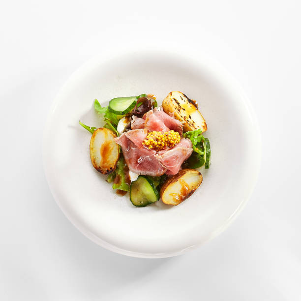 Salad with roast beef and vegetables. Delicious meat with cut potatoes and cucumbers in white plate. Tasty restaurant dish with seasonings and fresh greenery. Food presentation, haute cuisine