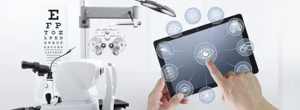 Photo of hands touch screen of digital tablet with ophthalmologist and optometrist icons symbols, ophthalmology and optometry equipment on background