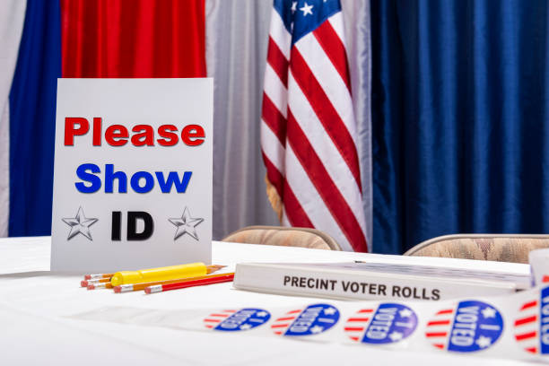 Empty US election registration desk with PLEASE SHOW ID sign A “PLEASE SHOW ID” sign on an empty registration desk at a US polling station on election day with red, white and blue bunting an American flag in the background. voter id stock pictures, royalty-free photos & images