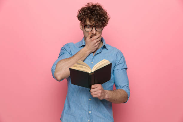 istock shocked guy holding hand to mouth and reading a book 1209878244