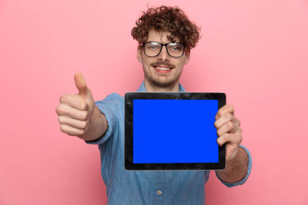 istock young casual guy making thumbs up sign and presenting tab 1209878582
