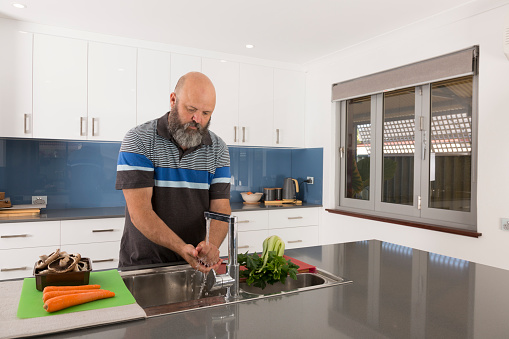 A man in his fifties washing his hands at the kitchen sink in preparation for cooking the family meal.