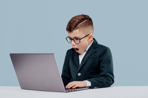 istock scared little schoolboy in suit and glasses  reading data from laptop while working on  project against blue background 1209885725