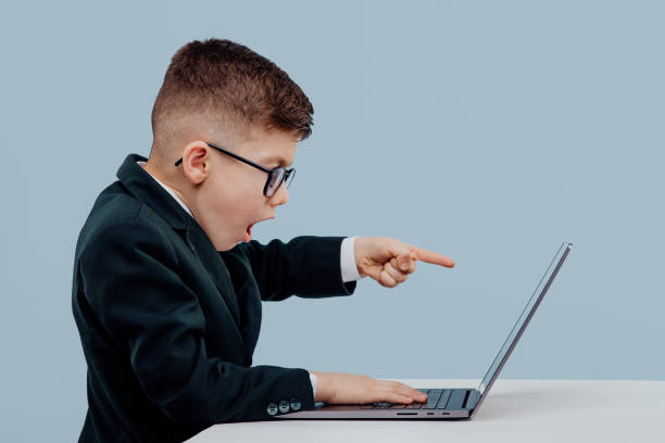 istock scared little boy in suit and glasses and reading data from laptop while working on business project against blue background, side view 1209885745