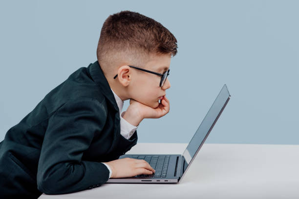 istock side view schoolboy. with glasses using a laptop, little boss in office funny kid, isolated on blue background, in studio 1209885746