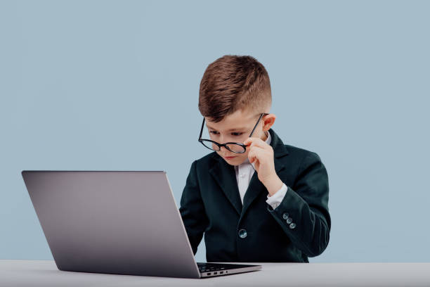 istock Little school kid with glasses using laptop on table isolated on blue background, in studio 1209885760