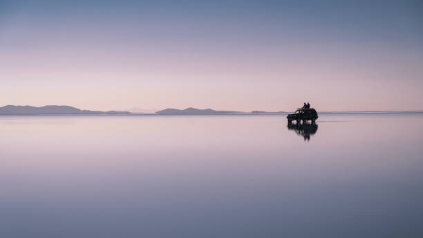 Travellers Exploring Uyuni Salt Flats at Sunrise in Bolivia, South America Young tourists sitting on top of 4x4 vehicle at sunrise at Uyuni Salt Flats (Spanish: Salar de Uyuni) in Bolivia, South America. salt flat stock pictures, royalty-free photos & images