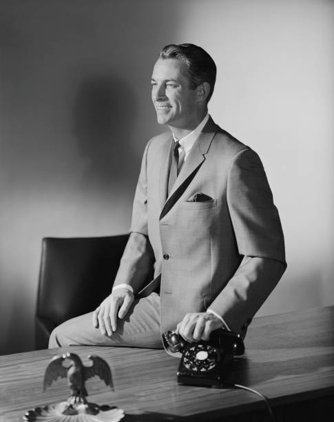 Businessman sitting on table holding telephone receiver  1964 stock pictures, royalty-free photos & images