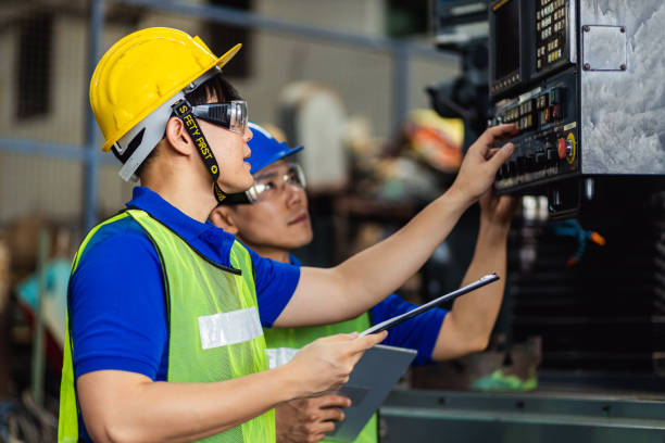 two men engineer talking in modern factory. production line machine and setting it for work. men industrial engineer wearing a yellow helmet while standing in a heavy industrial factory - building contractor engineer digital tablet construction imagens e fotografias de stock