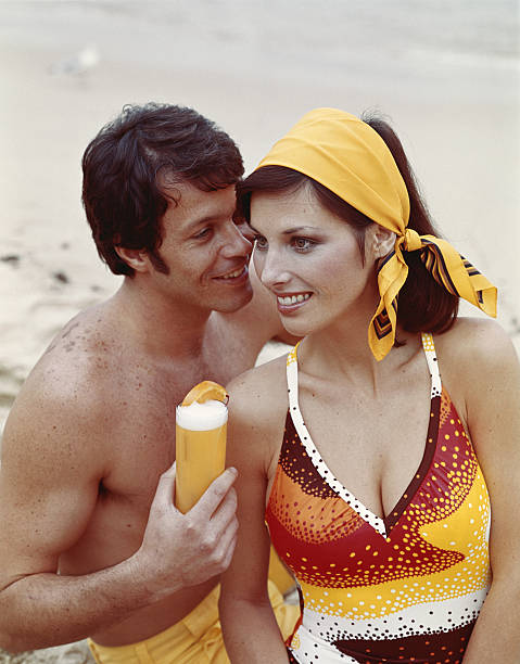 Young couple sitting on beach, smiling  1970s woman stock pictures, royalty-free photos & images