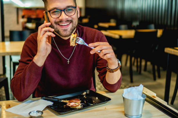 istock Young Man eating in restaurant and looking at mobile phone 1209893810