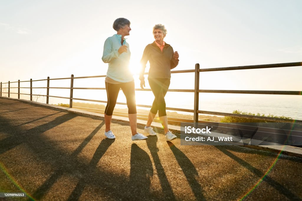 Morning walk is a blessing for the whole day Shot of two senior women walking together in morning with sun shining from behind Walking Stock Photo