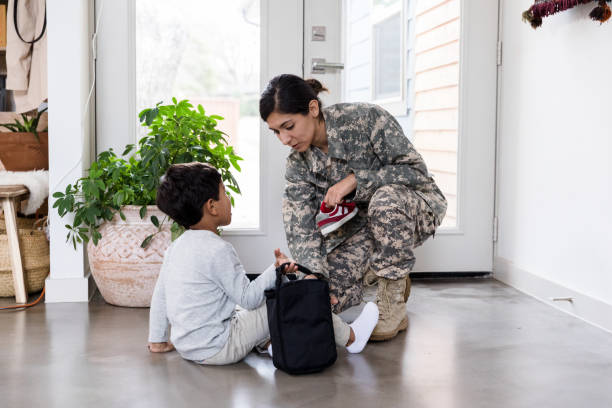 The mid adult military mom and her young son chat while she helps him put on his shoes before school.