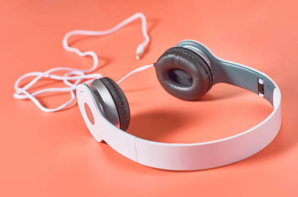 istock Modern white headphones with cable on orange background. Music concept 1209899030