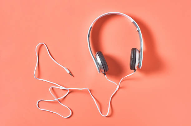 istock Modern white headphones with cable on orange background. Music concept. Top view 1209899035