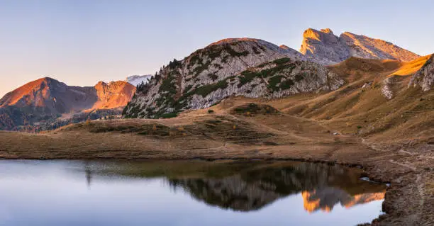 Early morning autumn alpine Dolomites mountain scene. Peaceful Valparola Path and Lake view, Belluno, Italy.   Picturesque traveling, seasonal, and nature beauty concept scene.