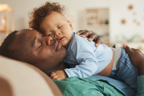 Father Cuddling with Baby Son Side view portrait of loving African-American dad embracing baby son while playing at home, copy space father and baby stock pictures, royalty-free photos & images