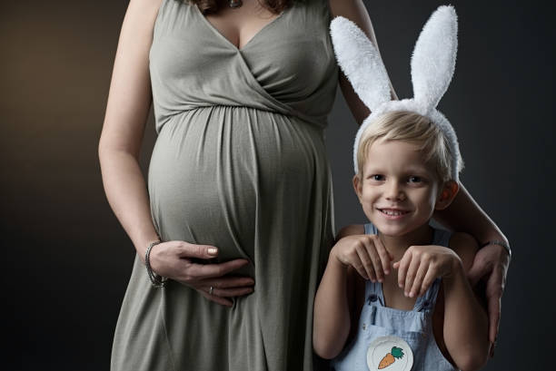 Close up shot of the pregnant woman with her smiling son in the bunny costume. Waiting for the baby. Motherhood. Easter. Image of the pregnant woman touching her big belly and baby boy in the bunny costume. Happy pregnant European woman with big tummy and her son. Pregnancy, motherhood, family, people and Easter concept olivia mum stock pictures, royalty-free photos & images