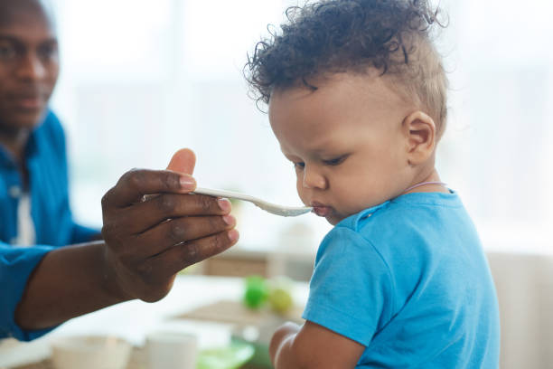 Mixed-Race Baby Refusing to Eat Side view portrait of cute African-American toddler refusing to eat food from spoon in kitchen interior, copy space refusing photos stock pictures, royalty-free photos & images