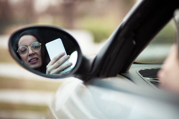 молодая женщина водит машину и пользуется телефоном - car phone стоковые фото и изображения