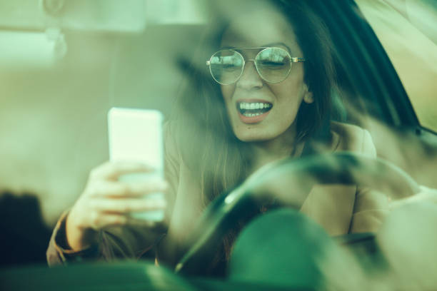 молодая женщина водит машину и пользуется телефоном - car phone стоковые фото и изображения