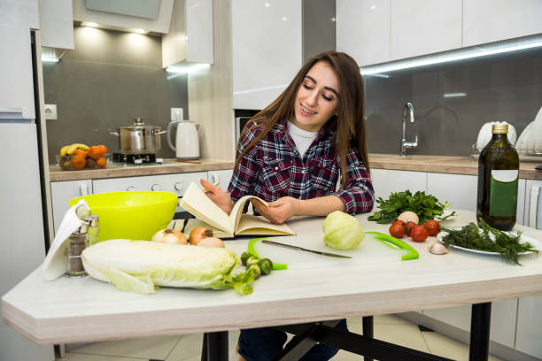 istock Young pretty woman sits at the kitchen table with different vegetables and writes or writes in her diary everything about healthy nutrition. 1209908417
