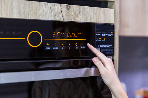 Close up of teenager's hand setting temperature control on oven.