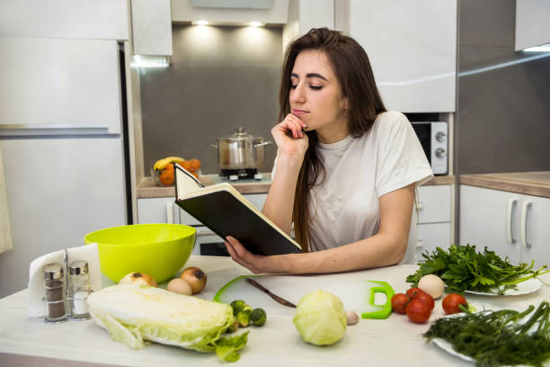 istock Young pretty woman sits at the kitchen table with different vegetables and writes or writes in her diary everything about healthy nutrition. 1209911708