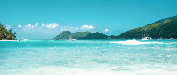 istock Panoramic view at ocean beach with yachts and tropical island at background 1209918668