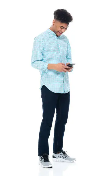 Photo of Generation z young male standing in front of white background wearing pants and using smart phone
