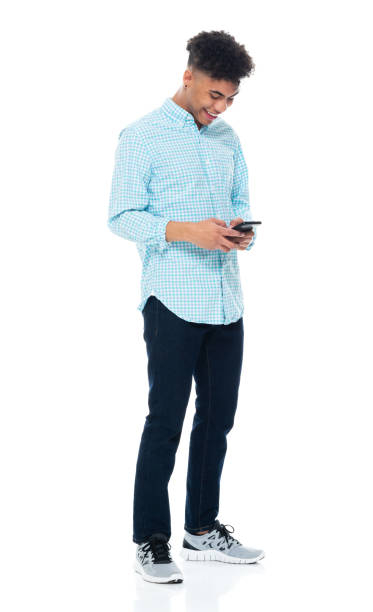 поколение z молодой мужчина, стоящий перед белым фоном в штанах и использующий смартфон - sleeve rolling rolled up rolled up sleeves стоковые фото и изображения