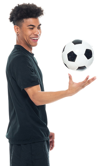 Profile view of aged 18-19 years old with black hair african ethnicity young male soccer player standing in front of white background wearing sports clothing who is serious and holding soccer ball and playing soccer - sport and using sports ball