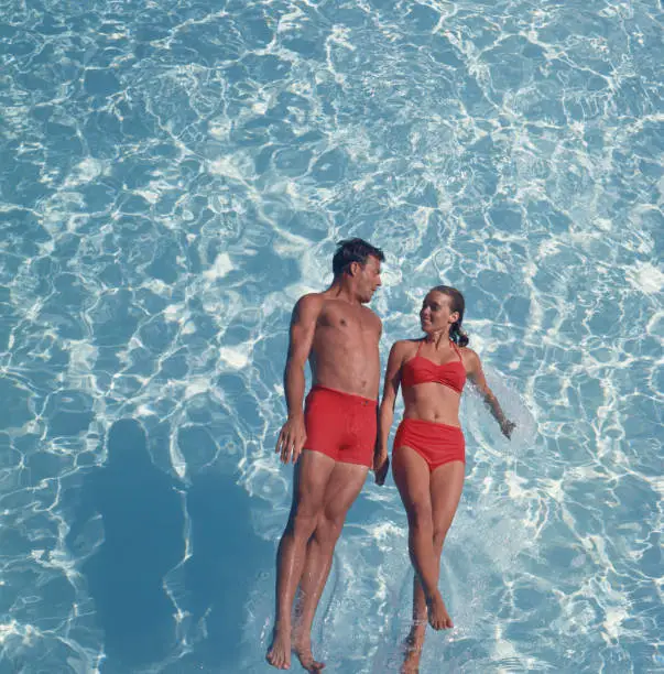 Photo of Young couple jumping in swimming pool, smiling