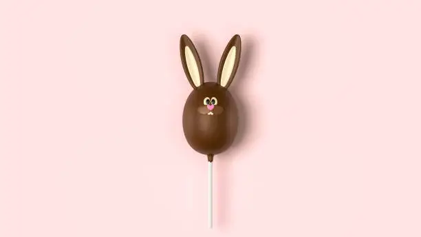 Photo of Chocolate Easter bunny, stick candy on pink background, top view. Sweet cute dessert, Easter holiday hunt symbol, milk chocolate rabbit, space for text. Traditional funny rabbit candy in shape of egg.