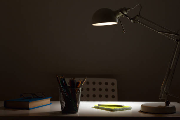 istock Workplace. The lamp in the dark with the light on, shines on the table 1209925882