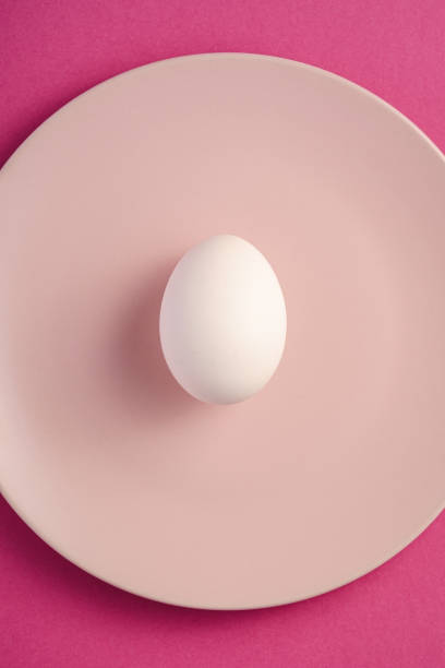istock White egg in pink plate on purple plain minimal background, top view, happy Easter day 1209926310