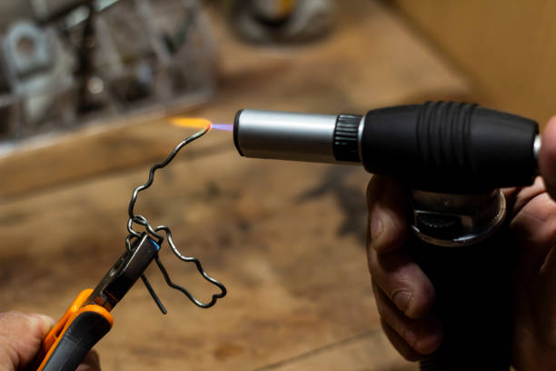 istock Old man working, using torch gun in his workshop, heating up some metal wire 1209929109