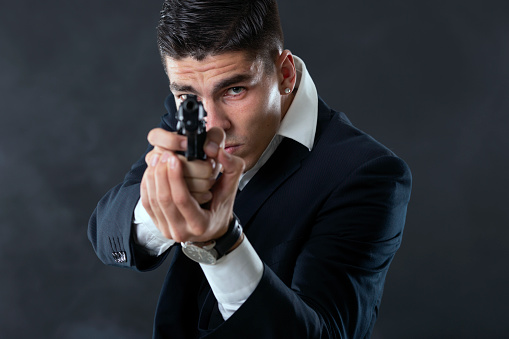 Young mafia man with a gun. About 25 years old Caucasian male in suit.