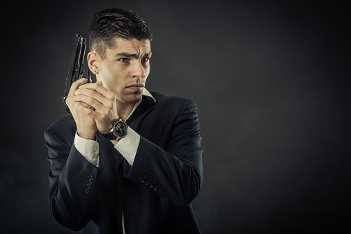 Young mafia man with a gun. About 25 years old Caucasian male in suit.