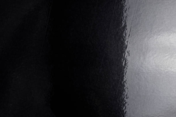 istock Black background made of real, shiny black paper covered with foil, illuminated by a soft light from the right. 1209940586