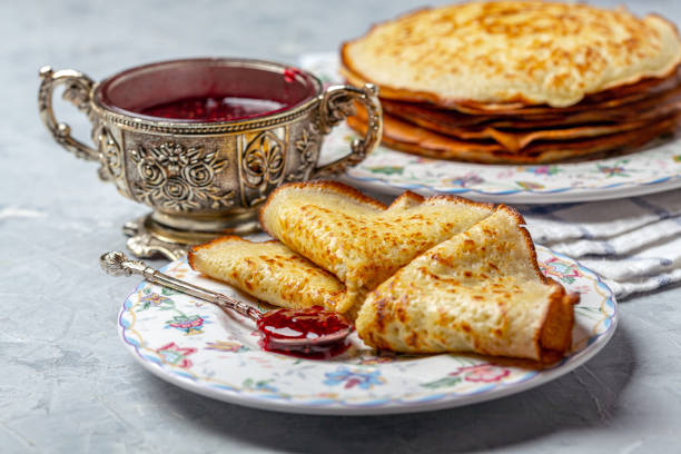 Crepes or thin pancakes are served on a plate with raspberry jam, selective focus.
