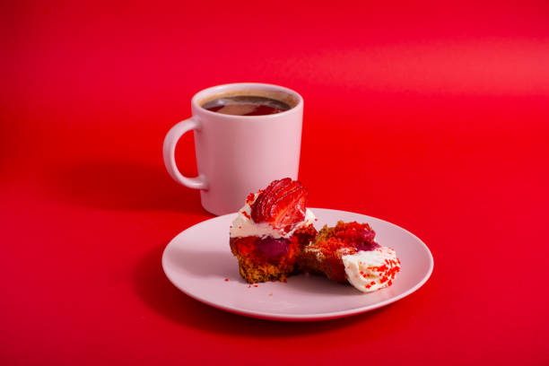 Pink cup of coffee and cupcake on a plate on a red background