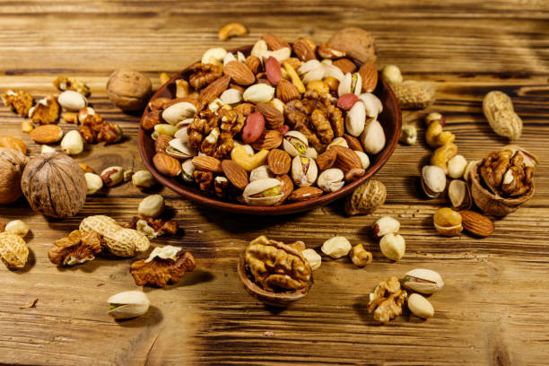 istock Mixed nuts on wooden table. Walnuts, pistachio, almond, peanut, cashew, hazelnut in ceramic bowl. Healthy eating concept 1209948788