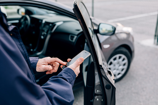 Male hands typing on cell phone. Unrecognizable mature man standing at rental car with smartphone.