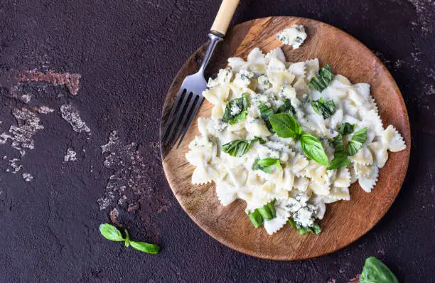 Pasta with creamy sauce with basil and gorgonzola cheese. Dark brown concrete background. Copy space.