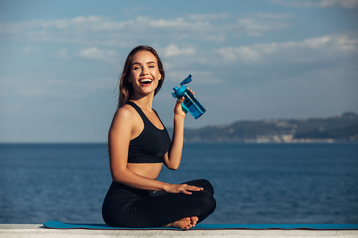 Fitness woman drinks water in front of sea background