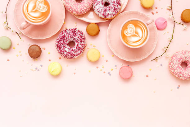 istock Two Latte Coffee cups, delicious pink donuts with sprinkle and colorful bright macaroons on pink paper background 1209961065