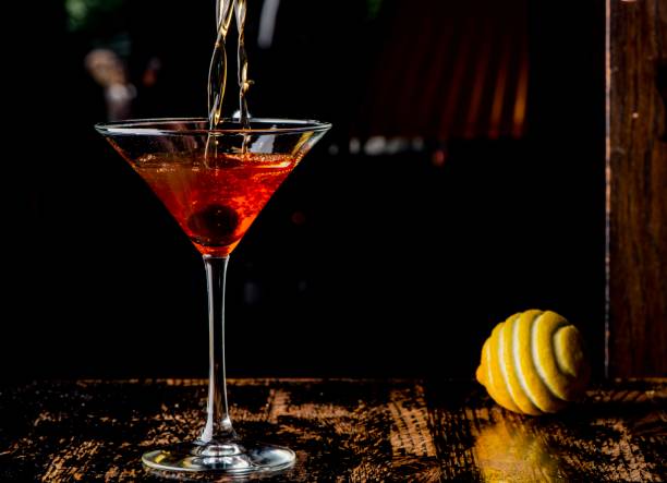manhattan, classico cocktail americano, a base di amaro di whisky di segale scosso e teso in un bicchiere martini e guarnito con una ciliegia imbevuta di bourbon e scorza di limone. - manattan foto e immagini stock